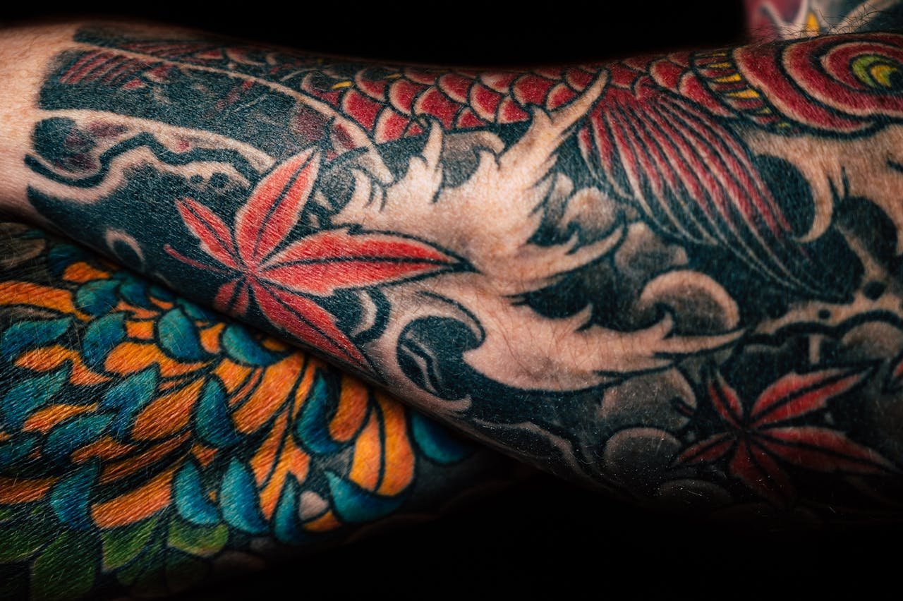 services-03 Detailed close-up of colorful sleeve tattoos featuring floral and abstract designs, showcasing artistic creativity.