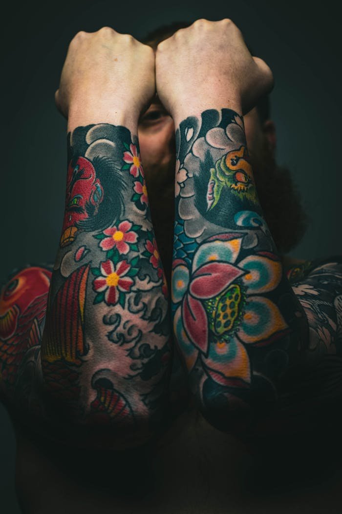 about-02 Vibrant forearm tattoos featuring flowers and koi fish showcased in an artistic pose.