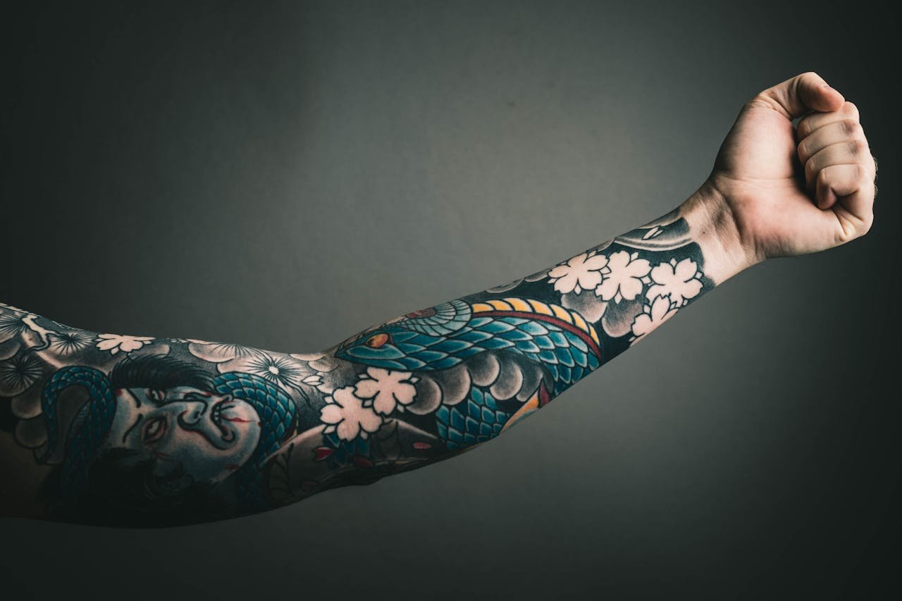 services-02 A close-up of a tattooed arm with a colorful sleeve design, featuring floral and artistic elements.